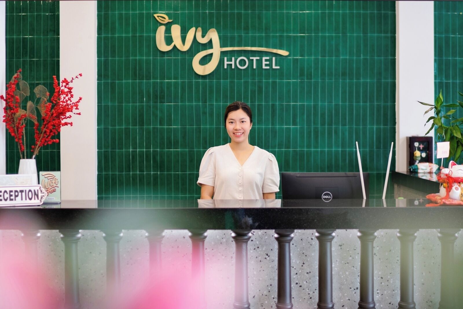 Un comptoir d’accueil à l’hôtel Ivy, avec un mur recouvert de carreaux verts, une enseigne indiquant « réception » et une plante.