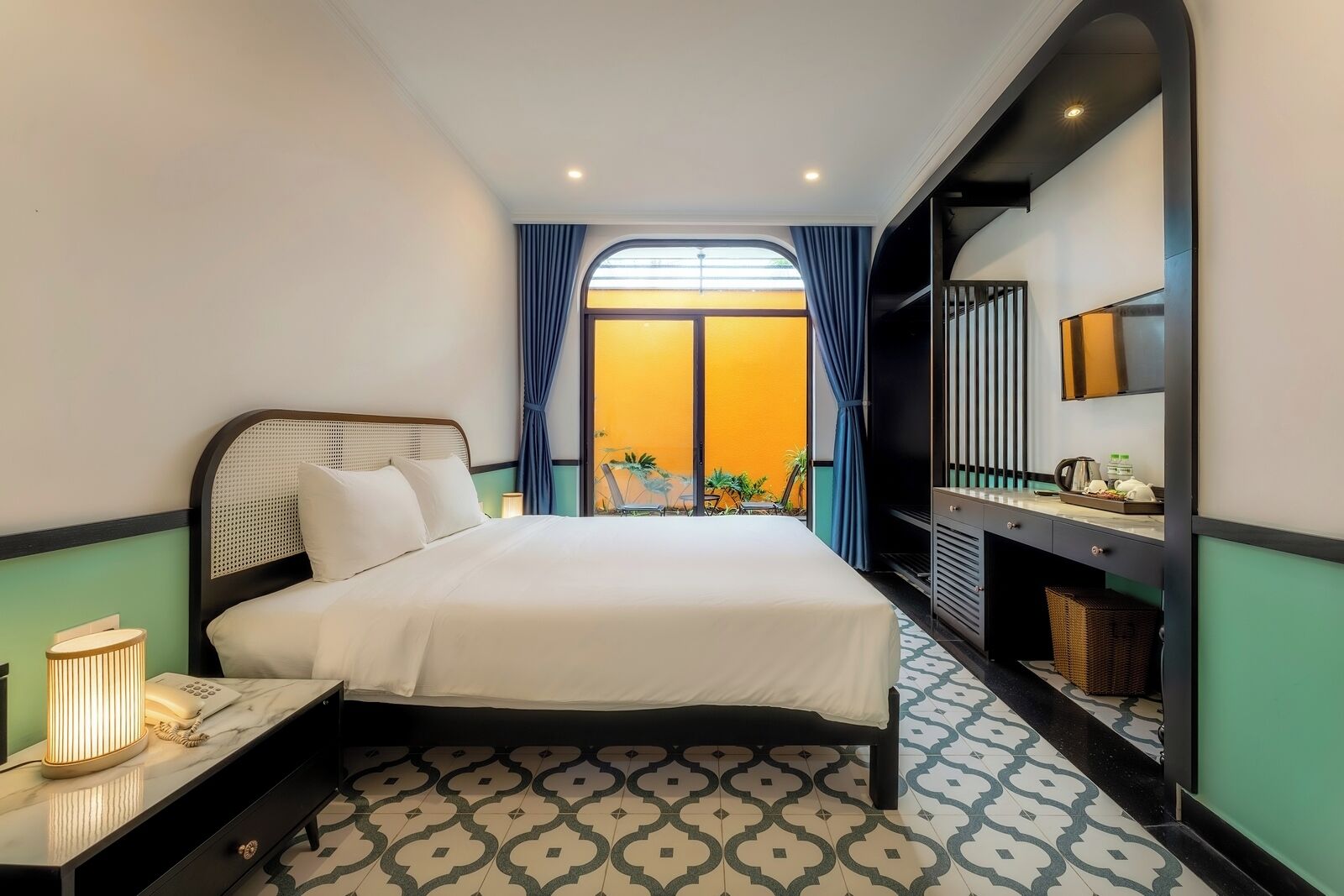 A hotel room with a bed, bedside lamp, and a view of the outdoors.