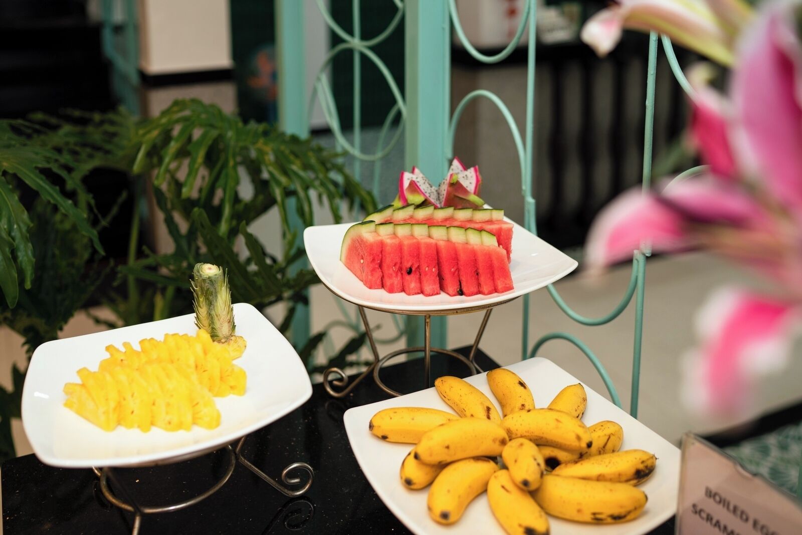 A table with three plates of food: pineapple slices, watermelon slices, and bananas.