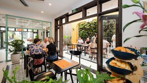An indoor dining area with tables, chairs, potted plants, and a view through large glass doors. - Hoi An Ivy Hotel (Da Nang)