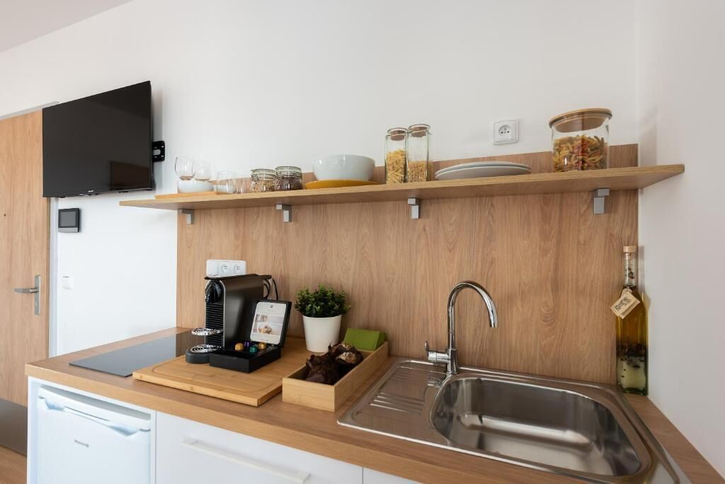 A modern kitchen with a built-in dishwasher, a coffee machine, a sink, and a TV mounted on the wall.