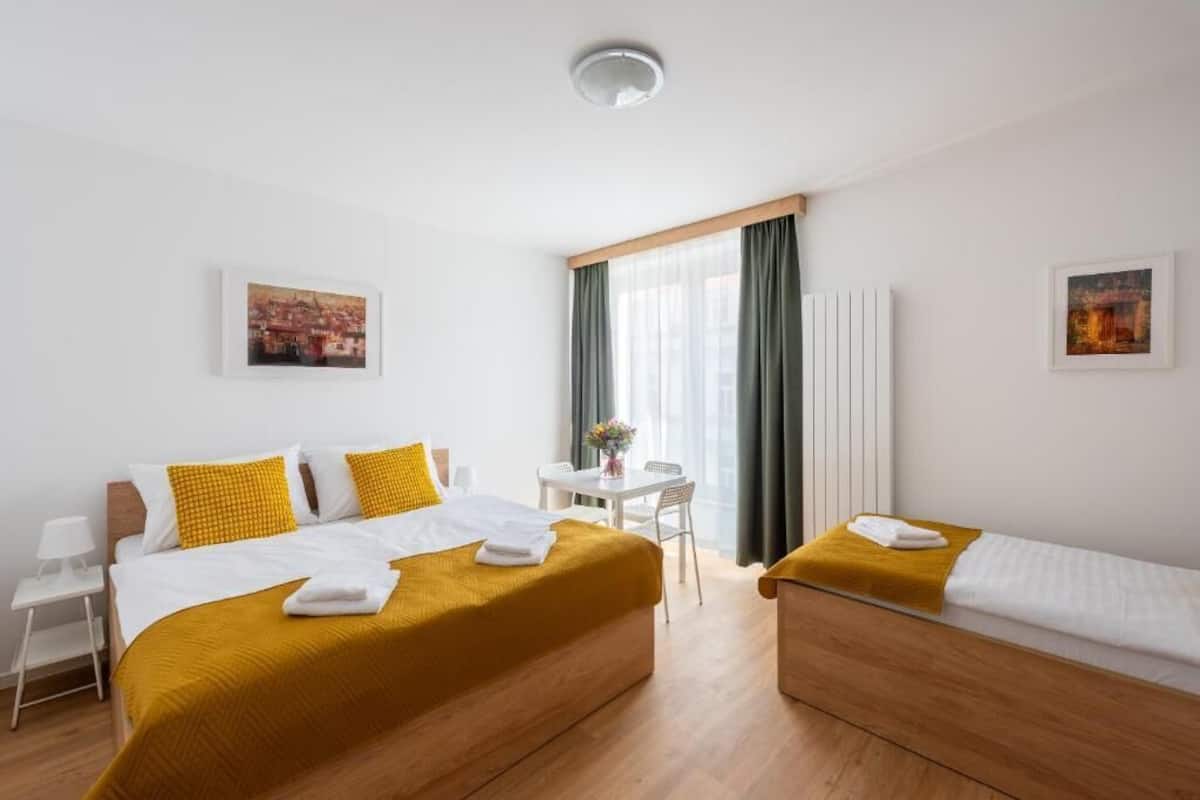 Une chambre d’hôtel avec deux lits, une petite table avec des chaises, une fenêtre avec des rideaux et des œuvres d’art accrochées aux murs.