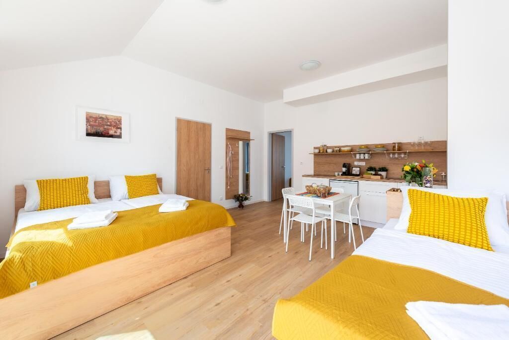 A modern hotel room with two beds, a kitchenette, a dining area, and a small bathroom.