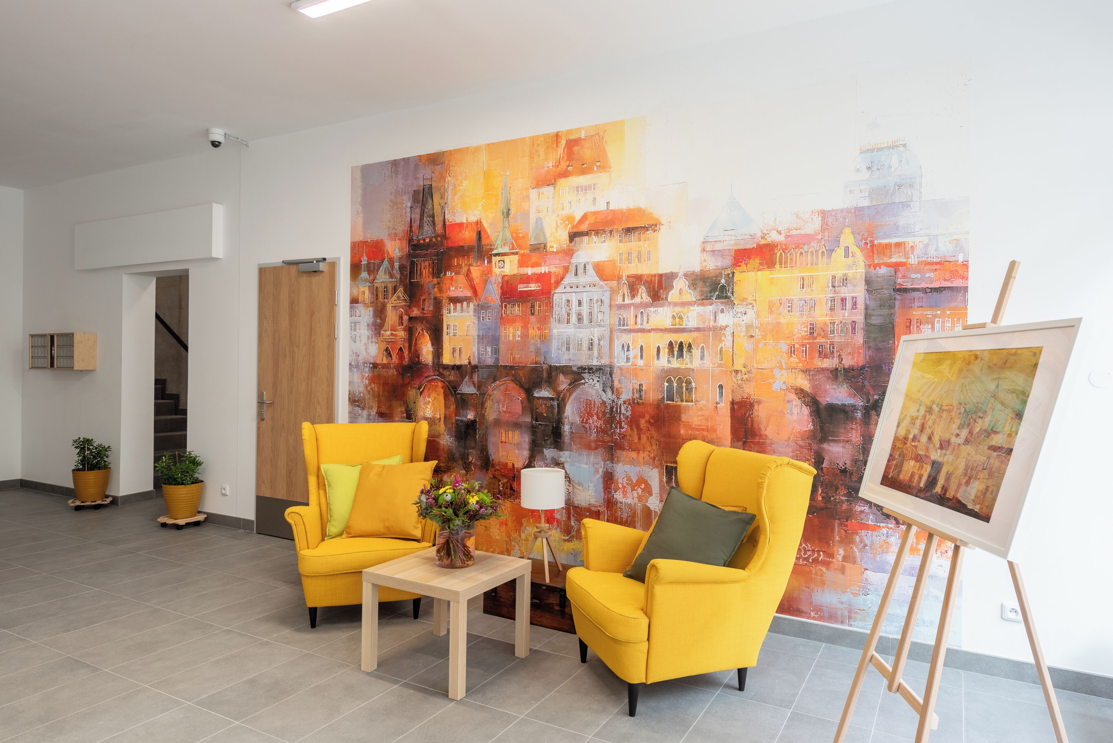 A room with two yellow armchairs, a small table with a vase of flowers, and a large abstract painting on the wall.