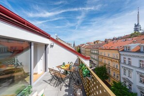 A balcony with a table and chairs, overlooking a cityscape with historic buildings and a tall tower. - Libero Apartments (Prague)