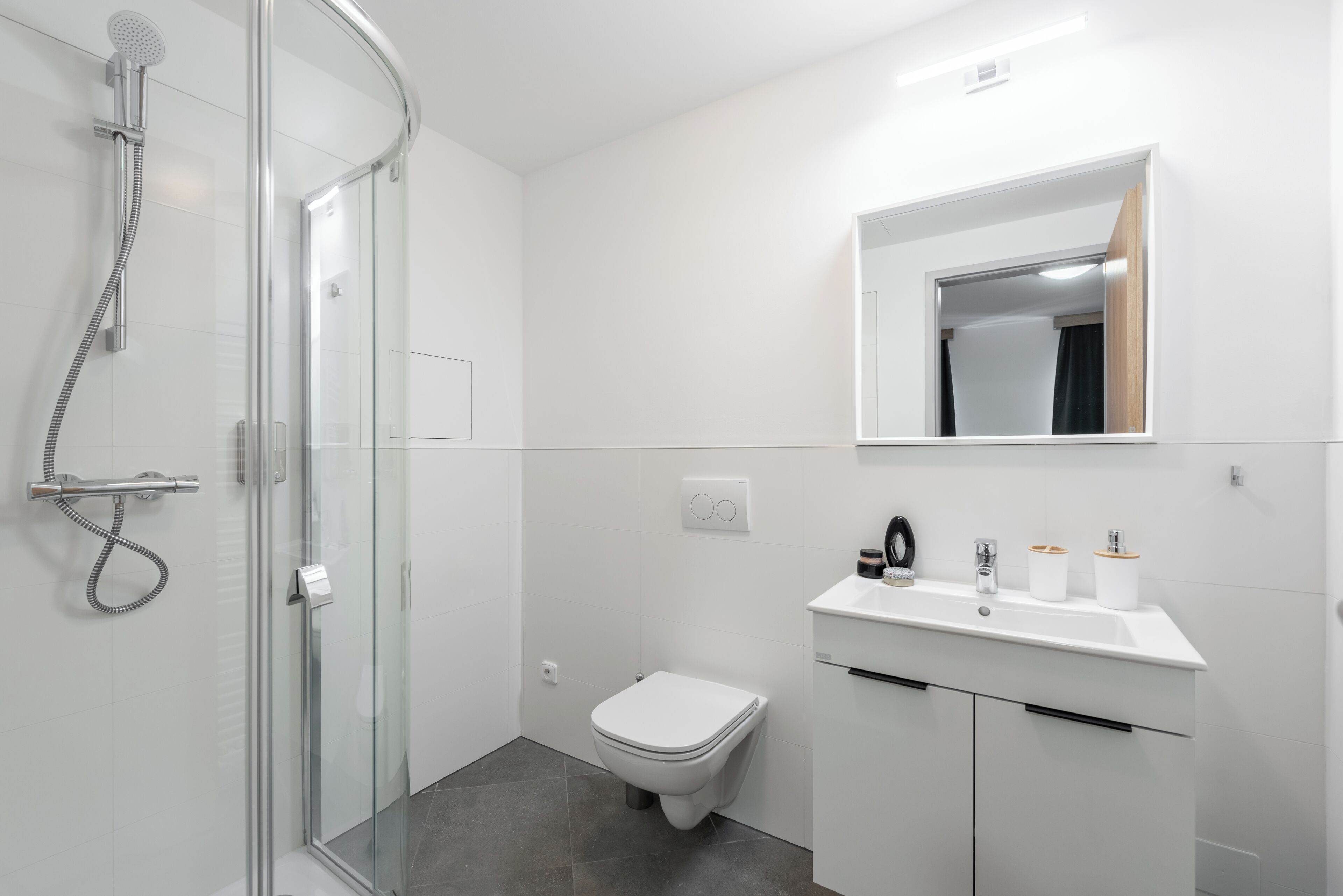 Une salle de bain moderne avec une douche à parois de verre, des toilettes blanches et un meuble-lavabo avec un miroir.