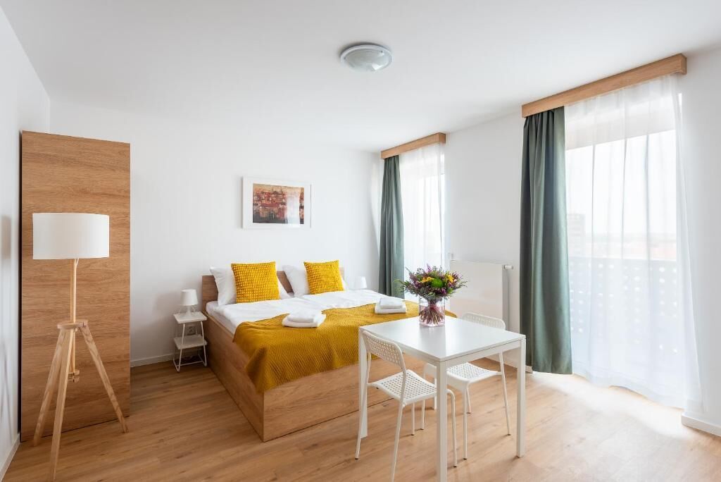 Habitación de hotel con cama, una mesita, lámpara, un cuadro en la pared y ventana con cortinas.