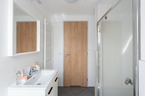 Un baño moderno con lavamanos blanco, espejo y puerta de madera.