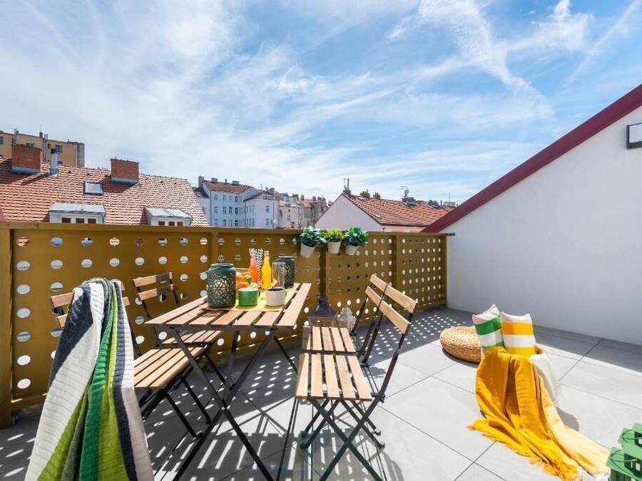 Una terraza en la azotea con muebles de madera, un paño amarillo y vistas de edificios al fondo.