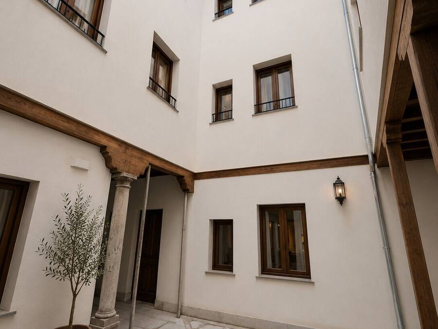 A courtyard with a fountain, potted plants, and a building with multiple windows and balconies.