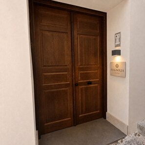 Puertas de madera dobles con un picaporte, un cartel en la pared que dice 'MAGNOLIA SUITES' y un pequeño letrero iluminado arriba.