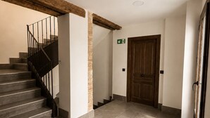 Un couloir avec un escalier, une porte en bois et un détecteur d’incendie au plafond.
