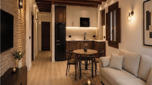 A modern kitchen with wooden cabinets, a black refrigerator, and a dining area with a round table and chairs. - Magnolia Suites by Blossom Hotels (Granada)