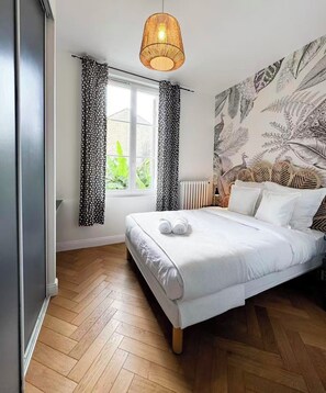 Une chambre à coucher avec un lit, une fenêtre avec des rideaux, un mur orné d’un motif de feuilles et un luminaire suspendu.