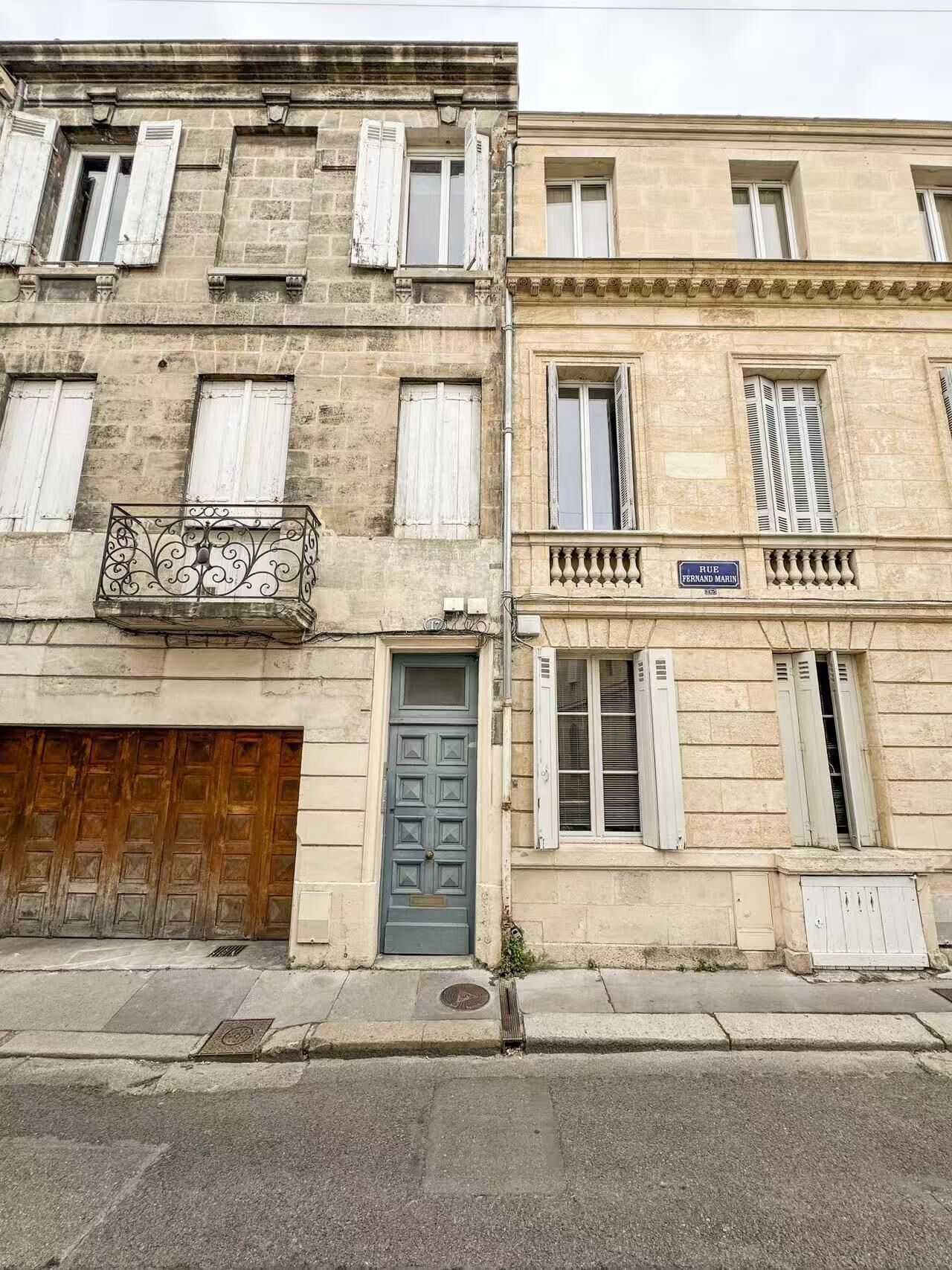 Un immeuble de deux étages avec une porte en bois, un balcon orné de balustrades en fer forgé et une enseigne indiquant « RUE FERNAND MARIN ».