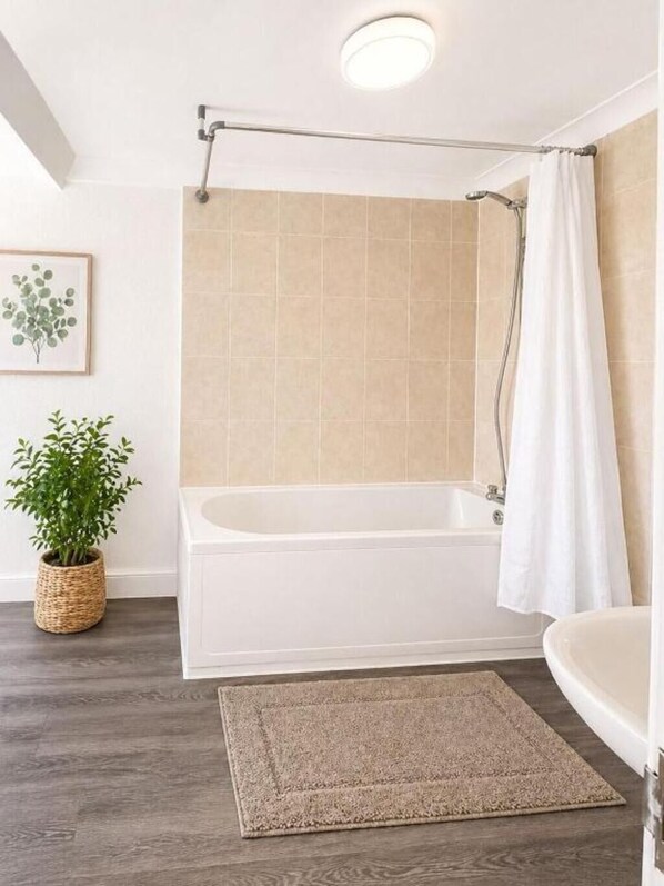 A bathroom with a bathtub, a shower curtain, a potted plant, and a framed picture on the wall.