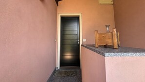 Un pasillo estrecho con una puerta de madera oscura, un pequeño banco de madera y un accesorio de luz en la pared.