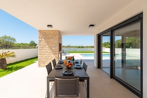 An outdoor dining area with a stone wall, a pool, and a clear view of the landscape. - Villa Antonio Zadarvillas (Nin)