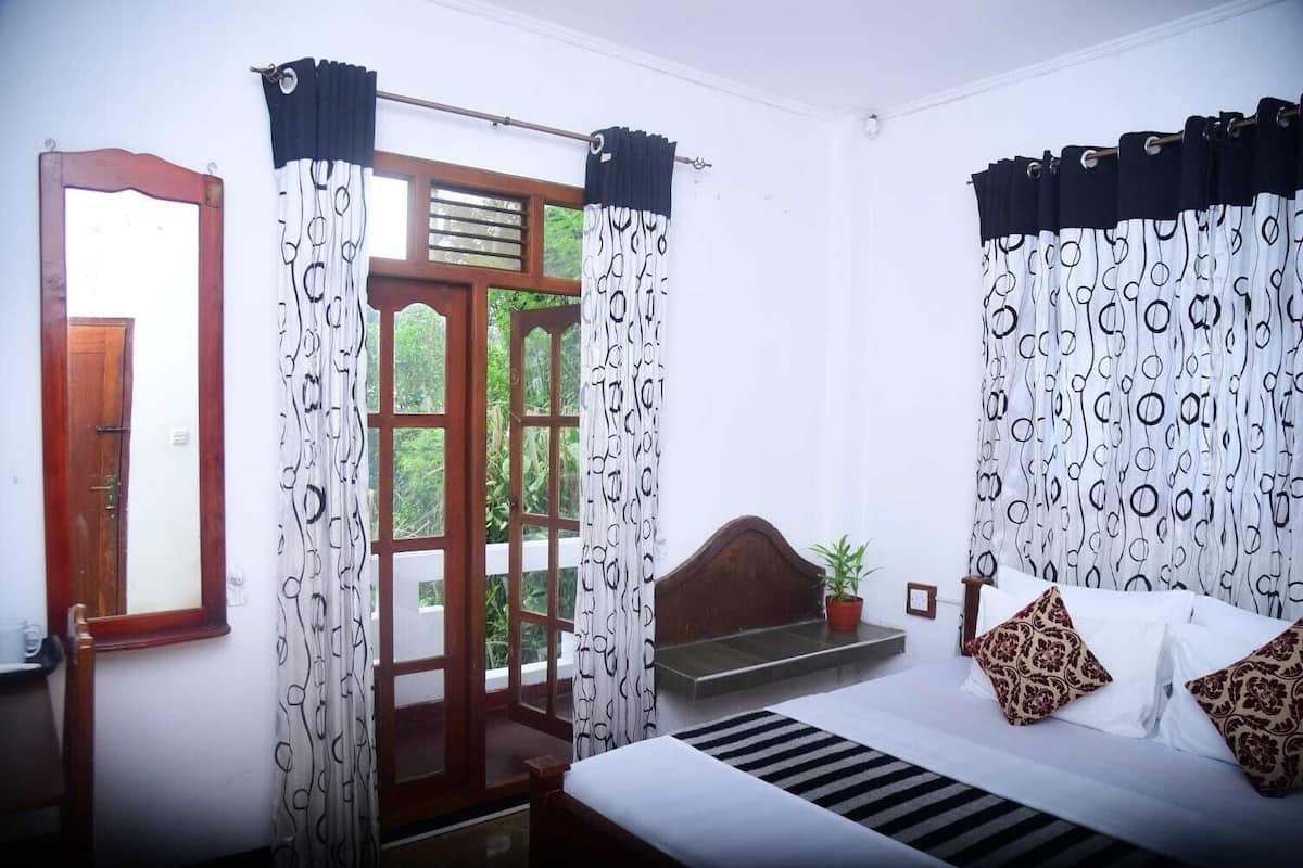 A bedroom with a bed, curtains, a window, and a view of greenery.