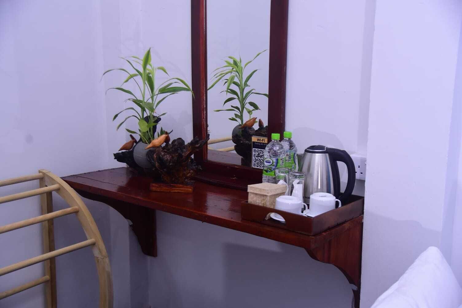 Un escritorio de madera con un espejo, dos plantas en macetas, una tetera, una cafetera y un cartel de Wi-Fi.