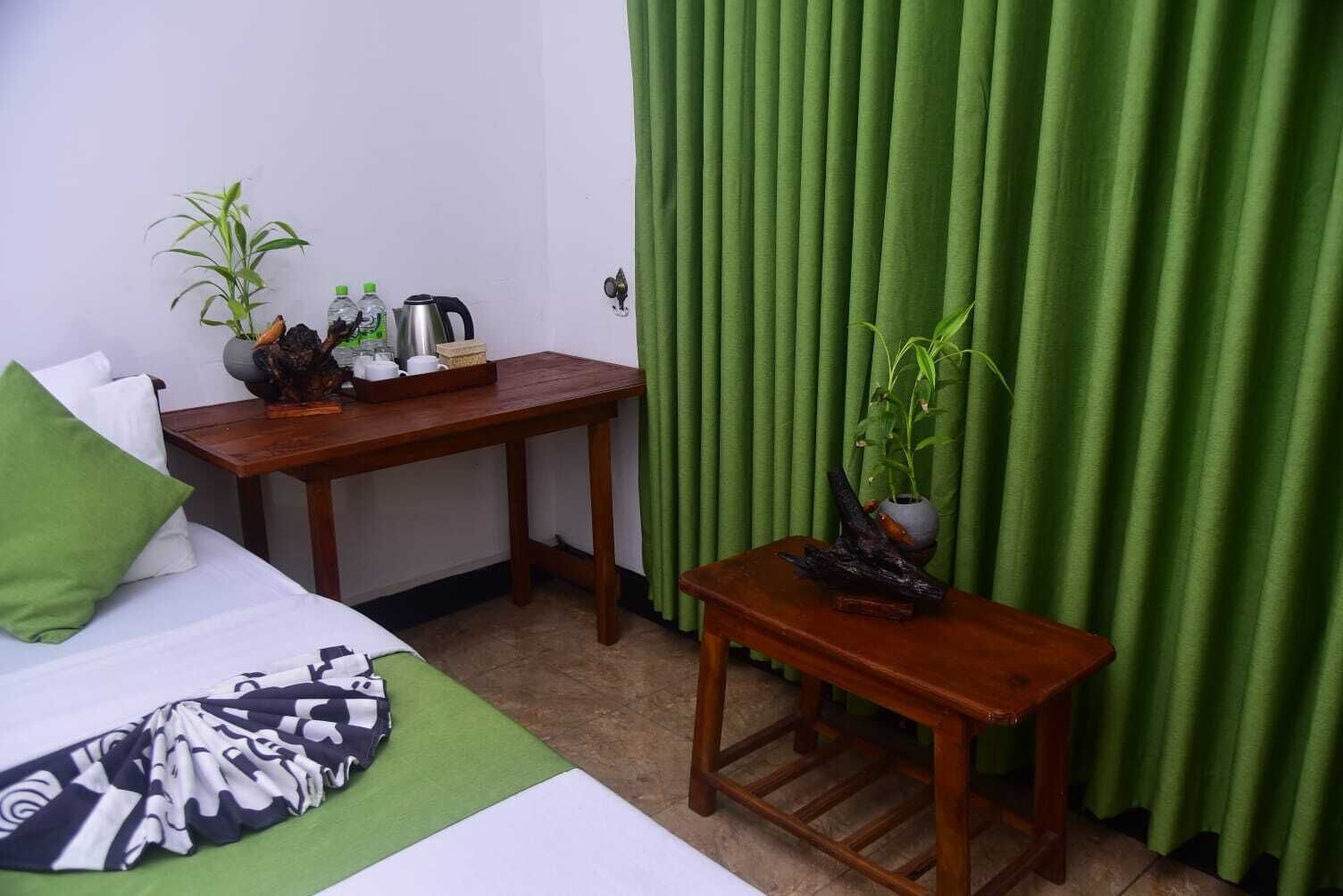 A hotel room with a bed, a small wooden table with a plant, a kettle, and a bottle of water.