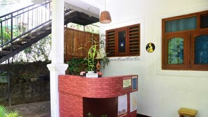 A reception desk with a brick counter, a staircase, and a wooden door with a window. - Travel Rest Inn (Ella)