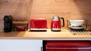 Una cocina con encimera de madera, un tostador rojo, una tetera roja, una cafetera y un bol blanco.