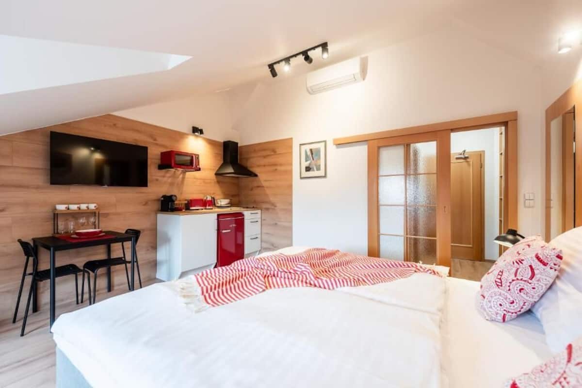 Ein Schlafzimmer mit einem Bett, einem Schreibtisch, einem roten Gerät und einem Fernseher an der Wand.