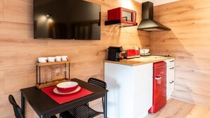 Una cocina compacta con televisión de pantalla plana, un microondas rojo y una cafetera.