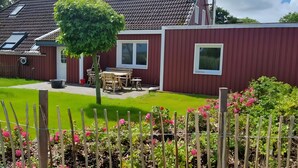 A red building with a patio, a table, and chairs. - Apartment 'Für 4 Personen 65 M²' with Private Terrace, Private Garden and Wi-Fi (Dornum)