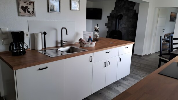 A modern kitchen with a wooden countertop, white cabinets, a built-in sink, and a black stove. - Apartment 'Für 4 Personen 65 M²' with Private Terrace, Private Garden and Wi-Fi (Dornum)
