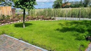 A well-maintained grassy yard with a stone border, a wooden fence, and a tree. - Apartment 'Für 4 Personen 65 M²' with Private Terrace, Private Garden and Wi-Fi (Dornum)
