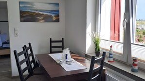 A dining area with a table set for two, a painting on the wall, and a view of the outdoors. - Apartment 'Für 4 Personen 65 M²' with Private Terrace, Private Garden and Wi-Fi (Dornum)