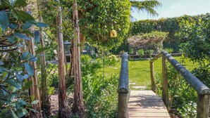 A wooden bridge in a garden with greenery and a clear sky. - Hydrangea Cottage (St Austell)