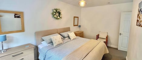 A bedroom with a bed, bedside table, lamp, dresser, and a door.