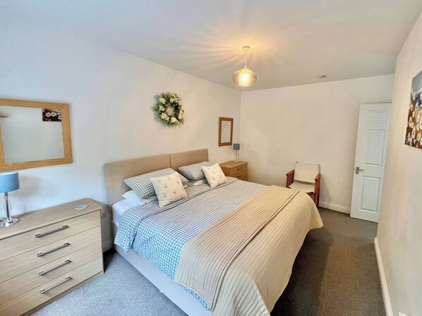 Un dormitorio con cama, mesita de noche, lámpara, cómoda y puerta.