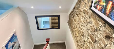 Una escalera con un muro de piedra, un cuadro enmarcado e iluminación empotrada en el techo.
