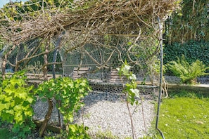 Um jardim com pérgola, chão de cascalho e diversas plantas.
