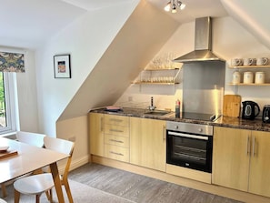A modern kitchen with wooden cabinets, a stainless steel range hood, and a built-in oven. - Hydrangea Cottage (St Austell)