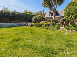 A stone house with a grassy yard, a wooden deck, and a stone wall. - Hydrangea Cottage (St Austell)