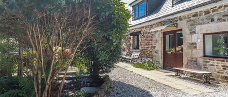 A stone building with a gravel driveway, a bench, and a tree.