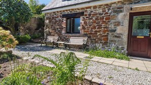 A stone building with a wooden door, a window, and a bench outside. - Hydrangea Cottage (St Austell)