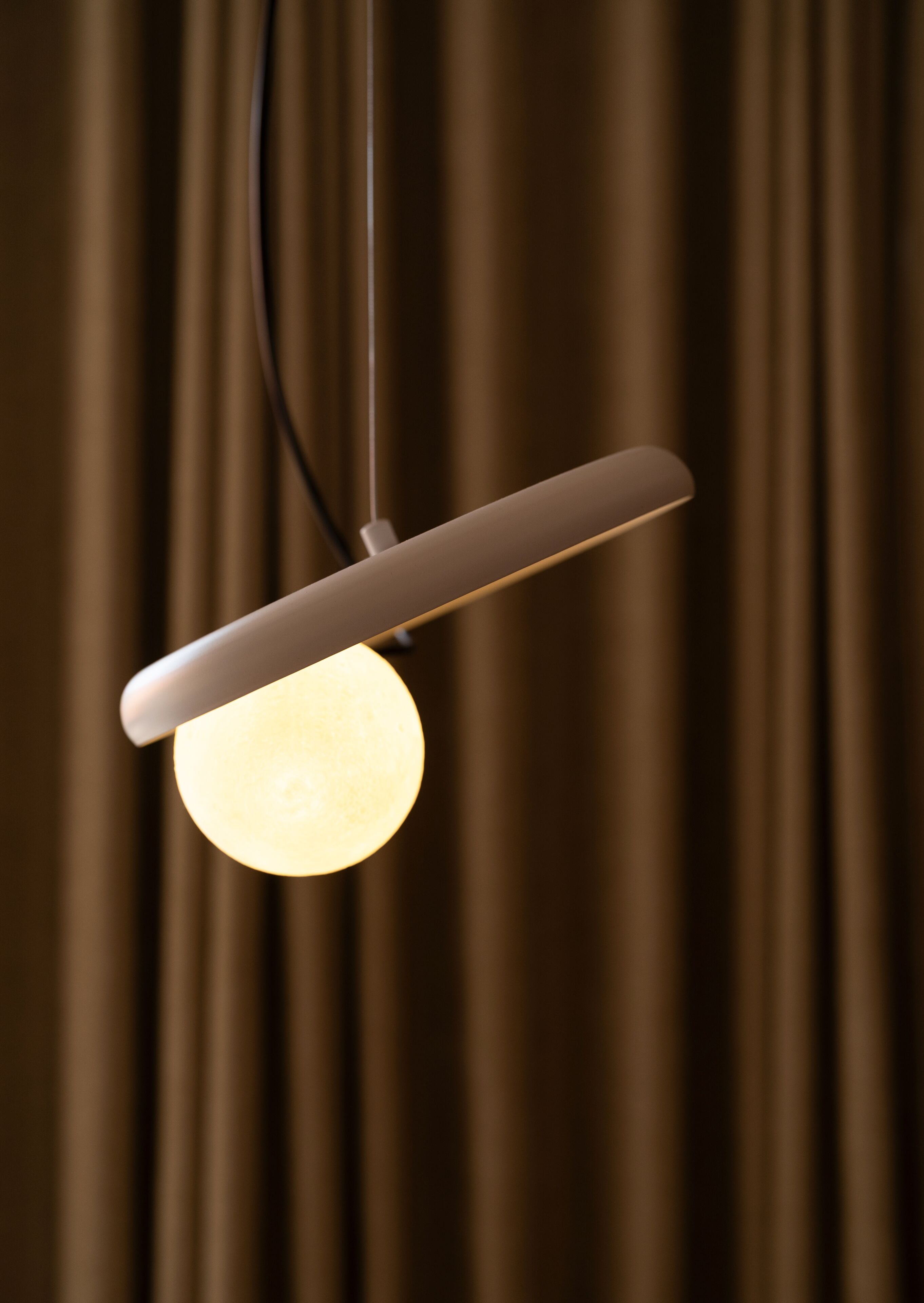 Un luminaire suspendu composé d’une ampoule sphérique et d’un abat-jour rectangulaire, le tout suspendu à un cordon.