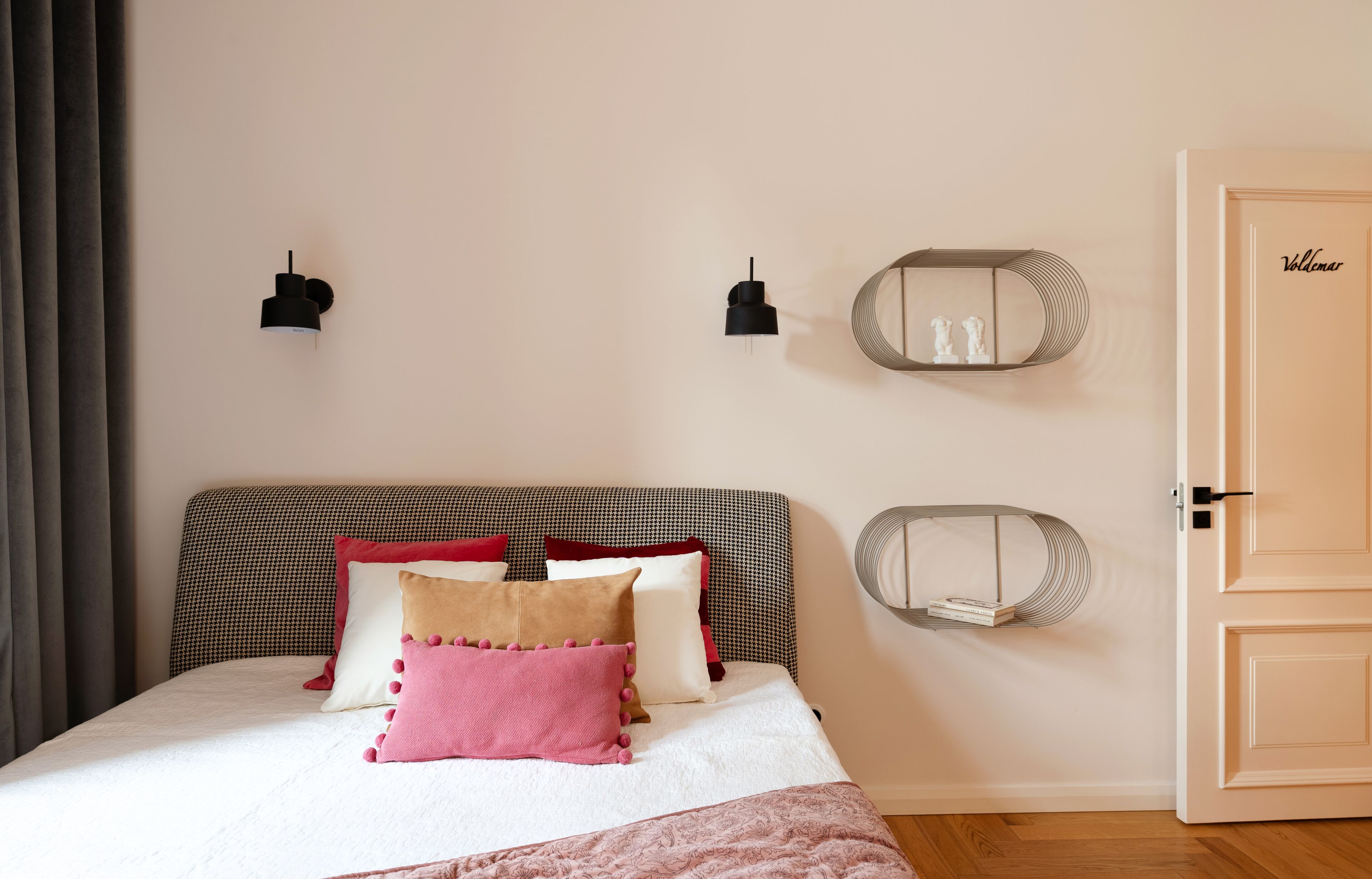 A bedroom with a bed, two wall-mounted lamps, a mirror, and a door.