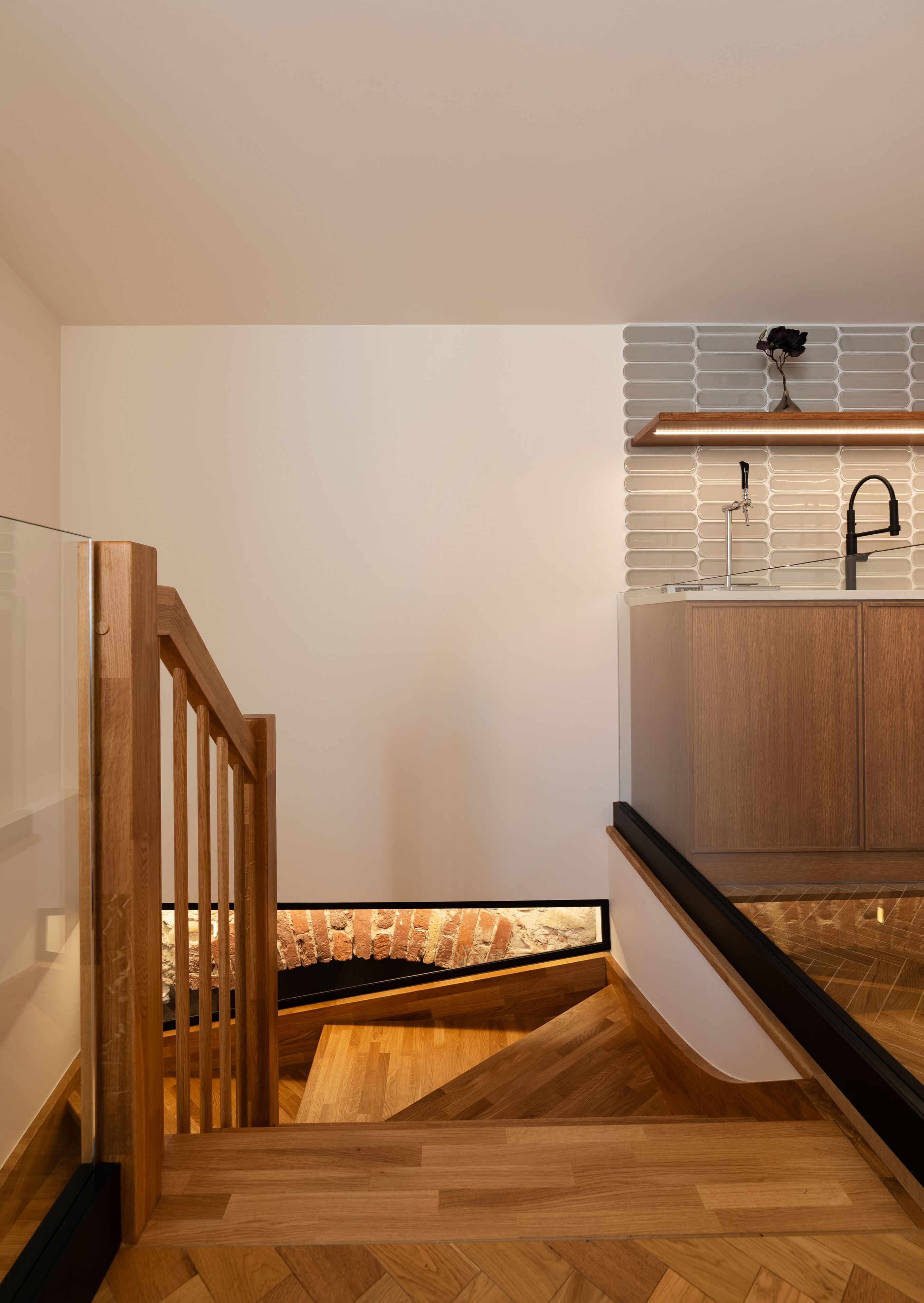 A modern kitchen with a wooden staircase, a black faucet, and a brick backsplash.