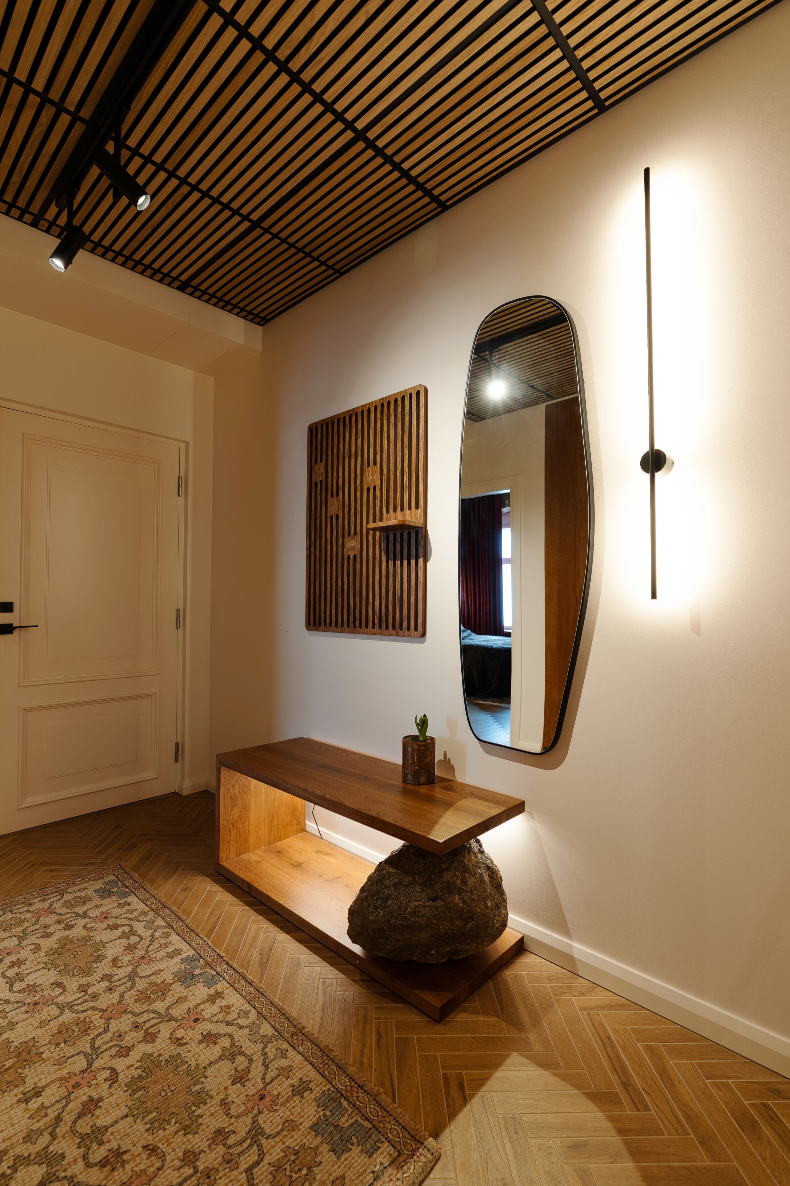 Un interno moderno con una panca in legno, un grande specchio e un tappeto decorato.