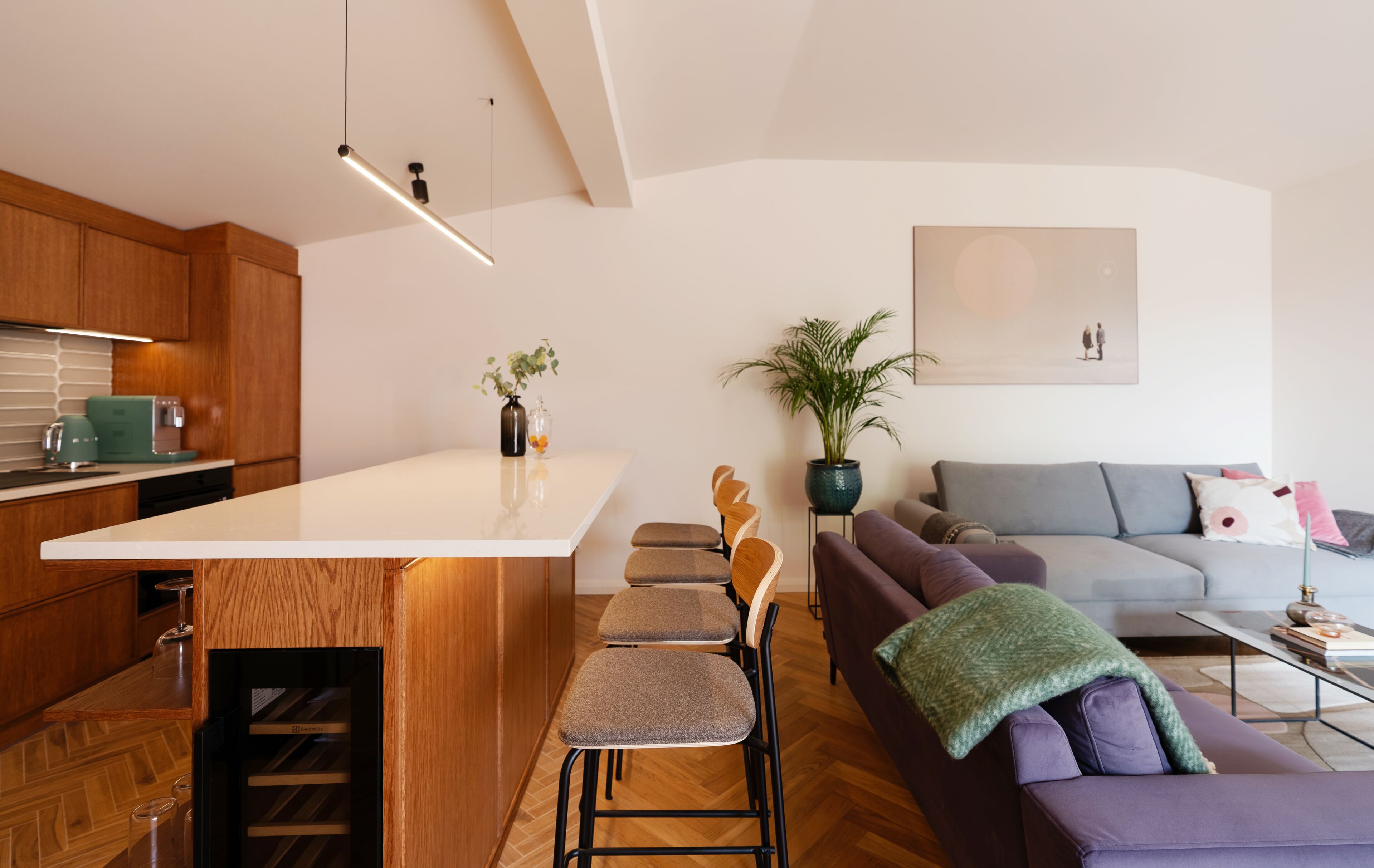 Een moderne keuken met een centraal eiland, houten kastjes en een zithoek met een bank en stoelen.