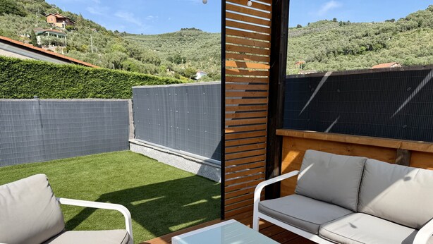 Une terrasse avec un canapé, des chaises et une table, entourée d’une clôture en bois et offrant une vue sur une colline.