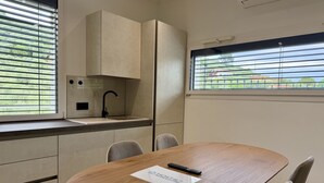 A modern kitchen with a built-in sink, a round wooden table, and a view of greenery through the window. - Dimora degli Ulivi C (Imperia)