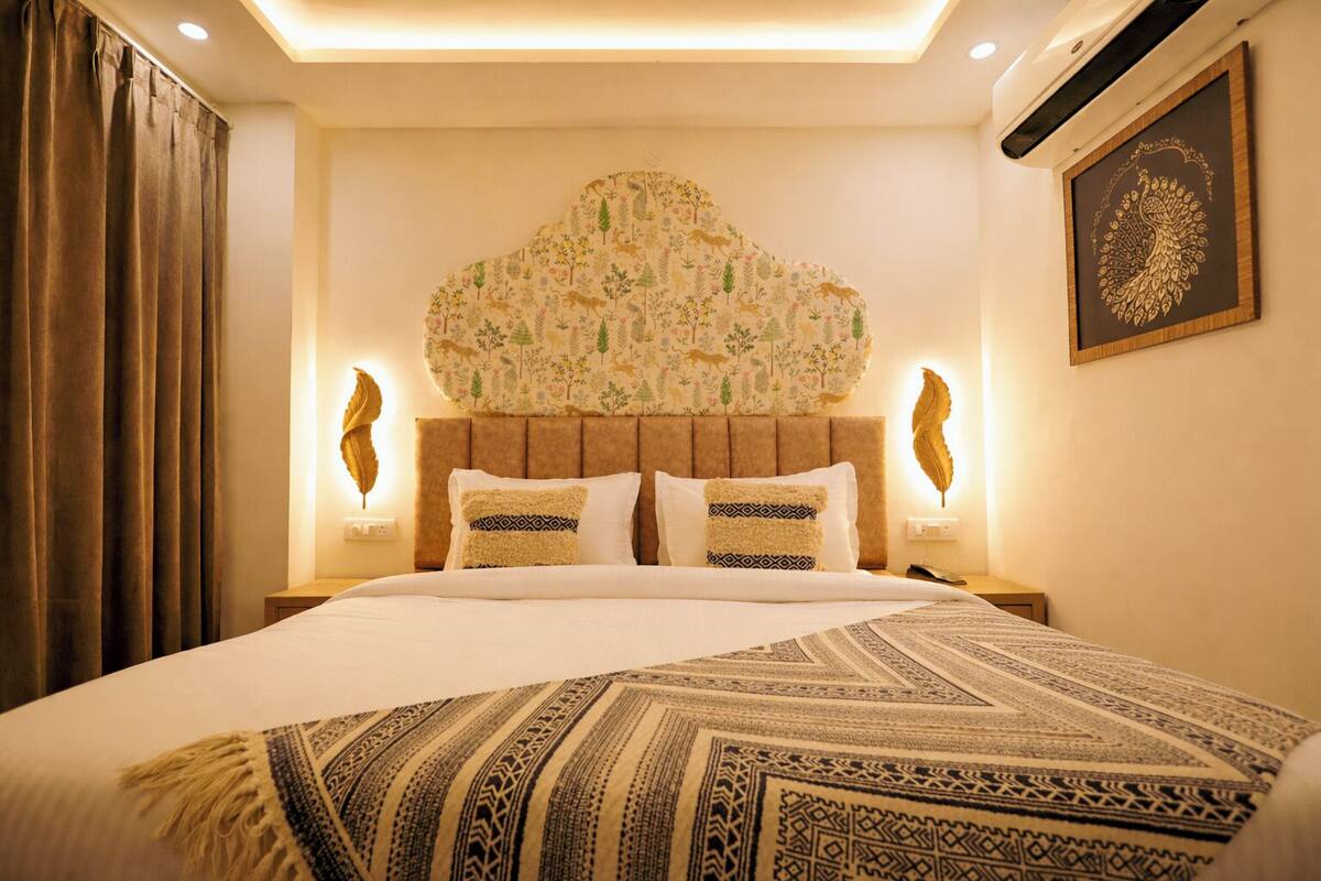 Una habitación de hotel con una cama grande, un cabecero decorativo, dos lámparas de noche y una obra de arte colgada en la pared.